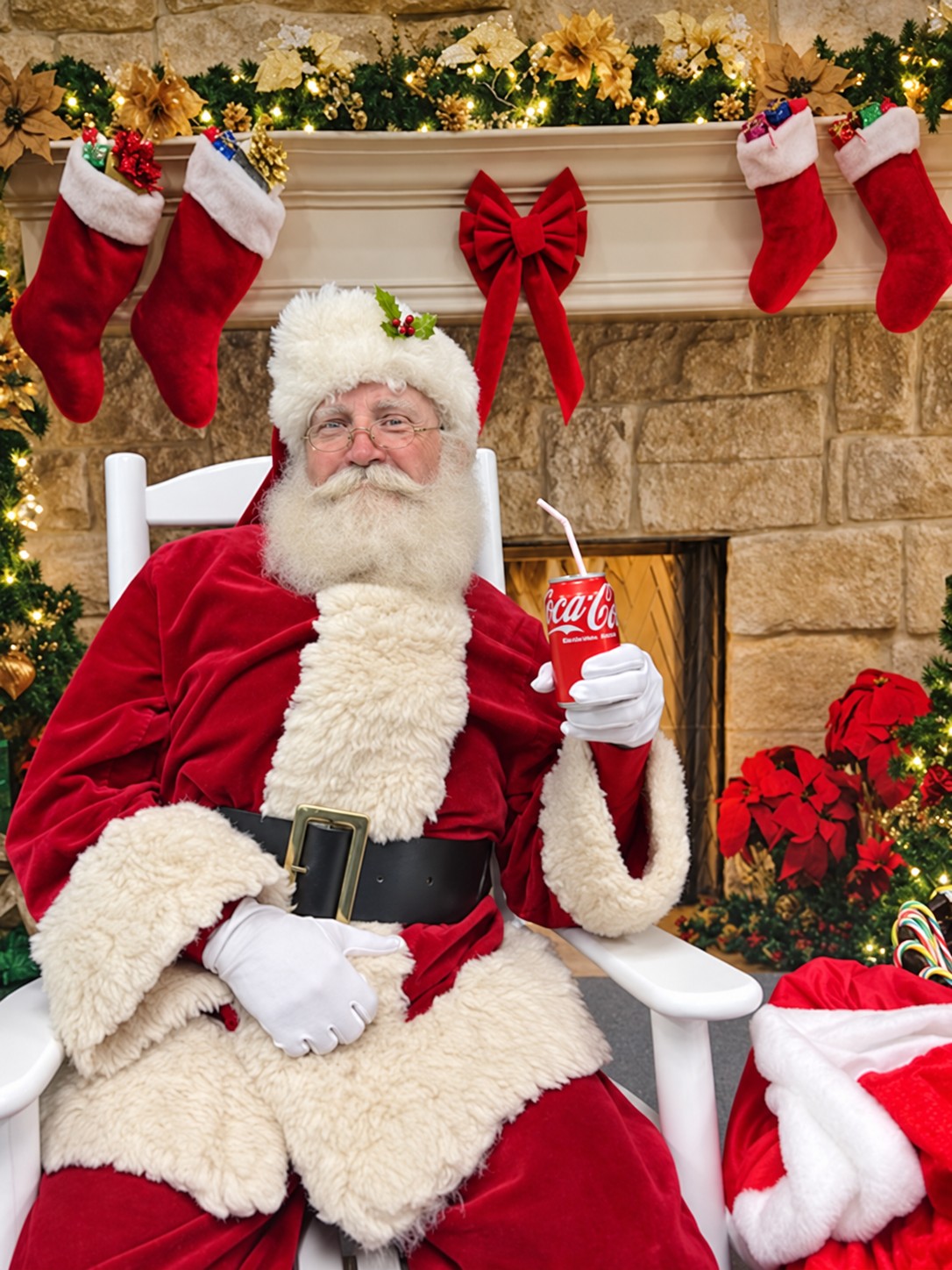Santa seated beside a decorated fireplace holding a soft drink