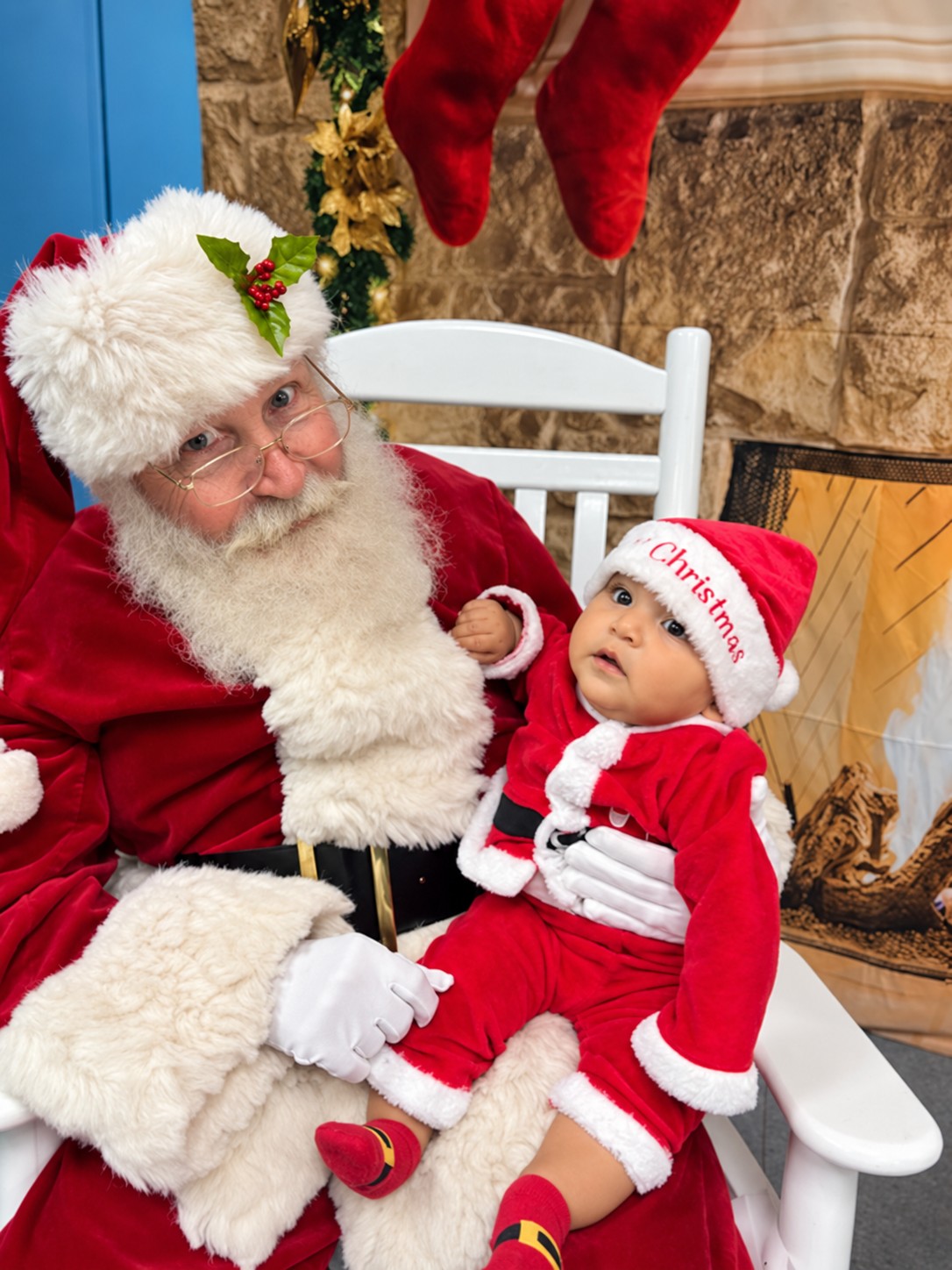 Santa holding a baby dressed in a red Christmas outfit