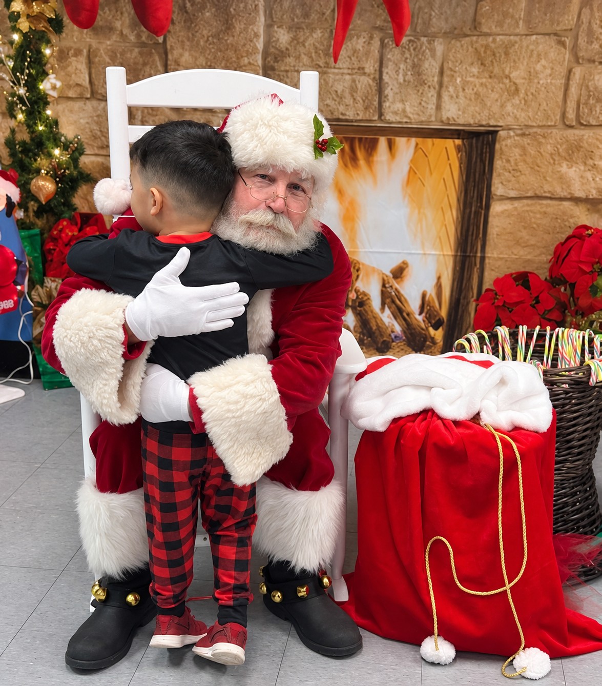 A young guest giving Santa a hug beside a Christmas gift sack